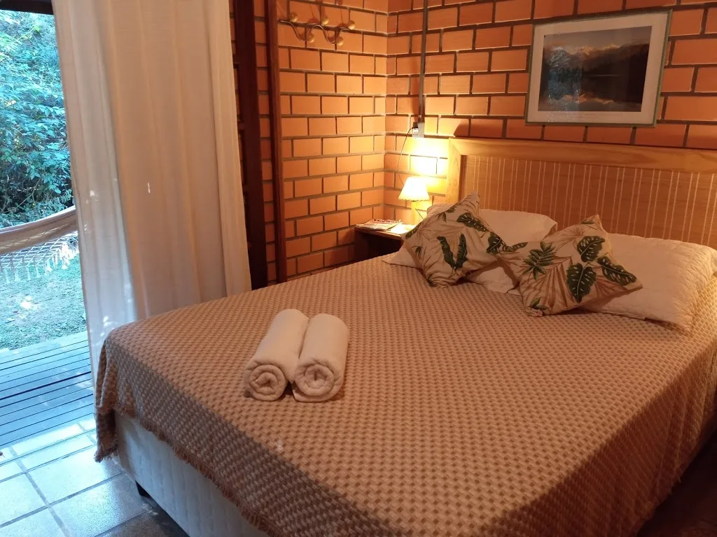 Suíte de casal com porta de vidro voltada para o jardim da pousada