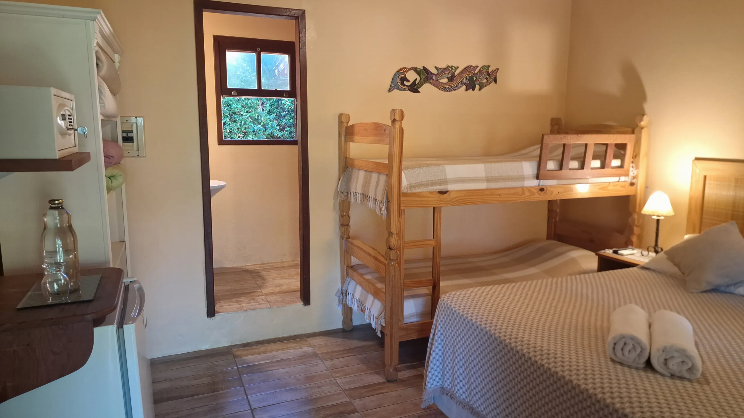 Suíte 9 com cama de casal, beliche de madeira e a porta do banheiro