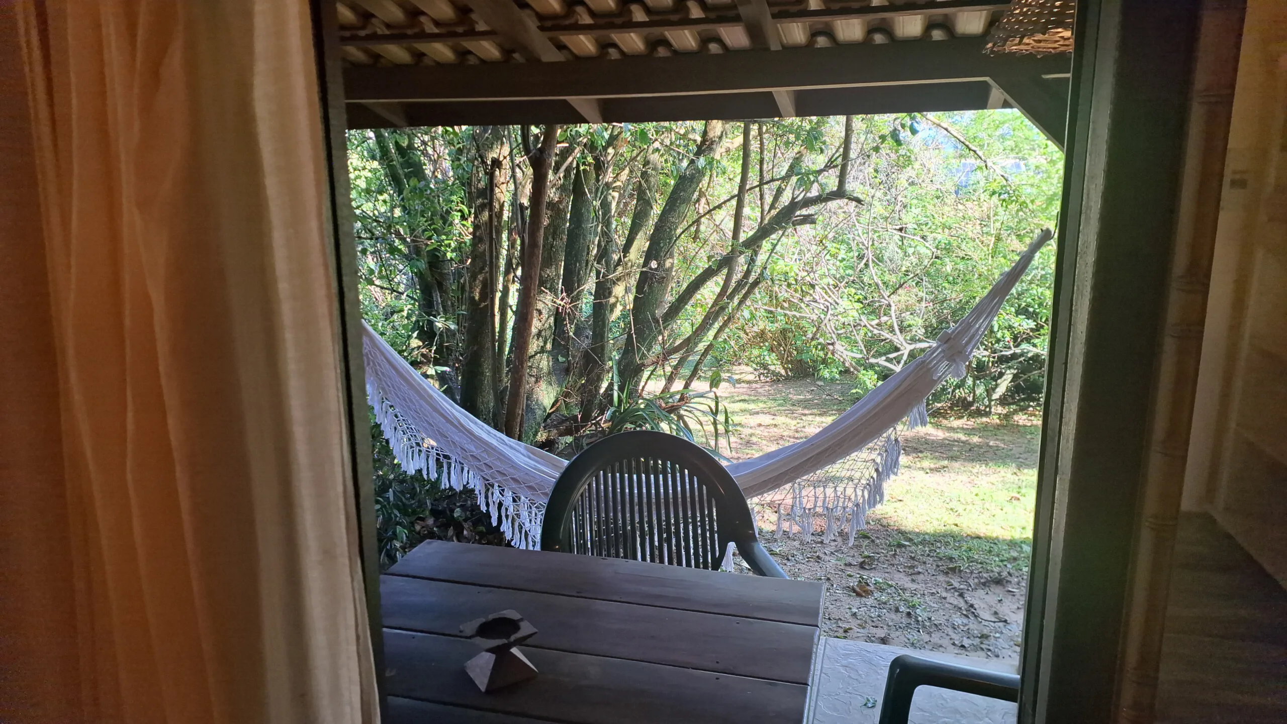 Vista da janela da Suíte 9 para a varanda com rede e o jardim