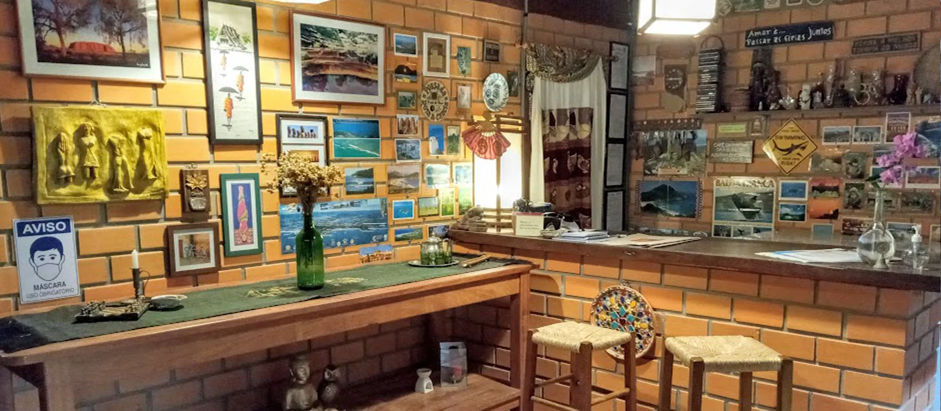 Bar e recepção da pousada com parede de tijolinho e quadros