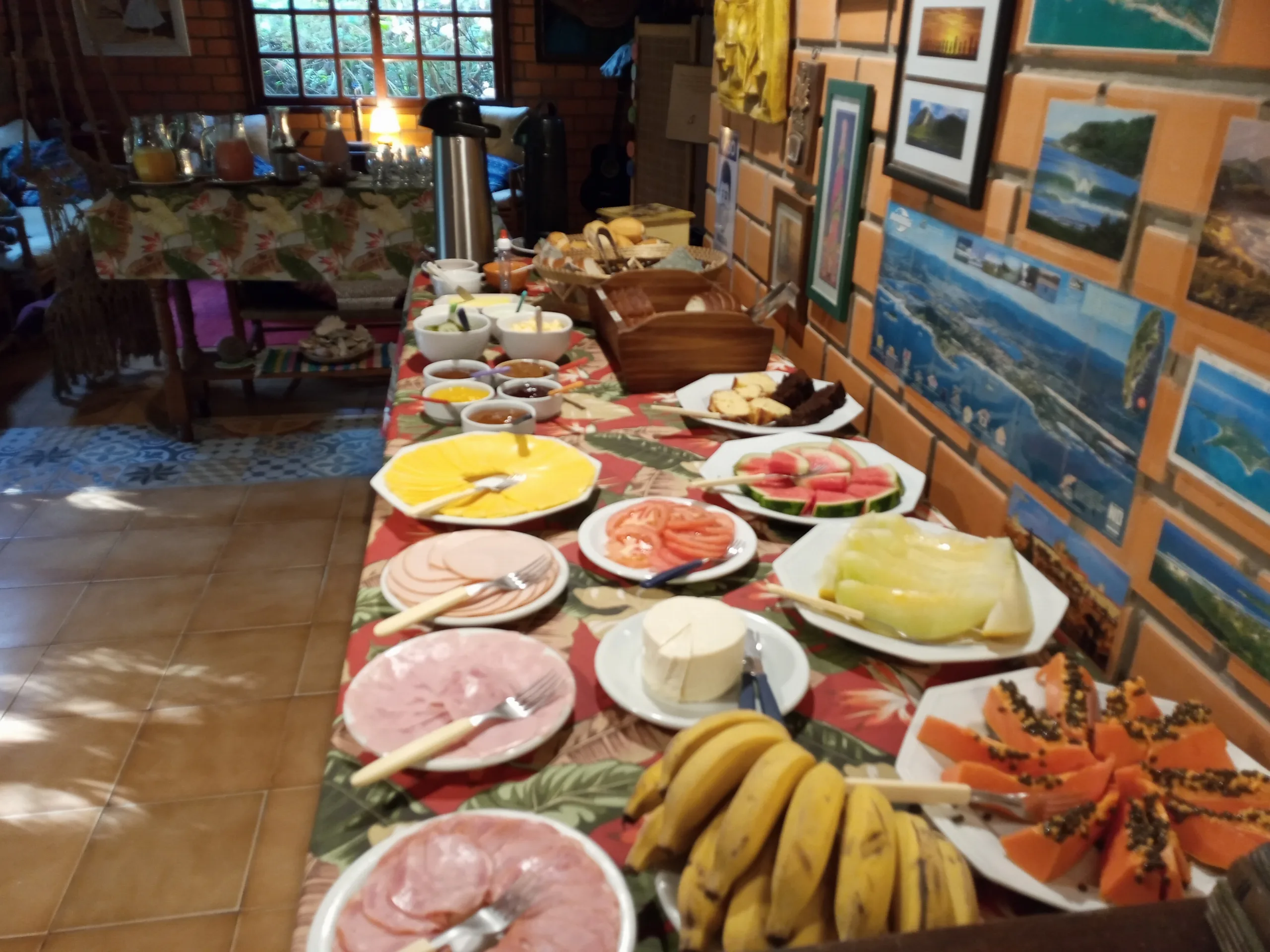 Café da manhã colonial servido no salão, com frutas, frios, queijos e bolos