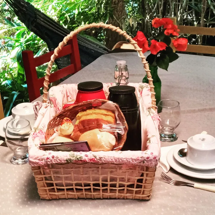Cesta de café da manhã com pães, bolos e garrafas térmicas sobre a mesa posta