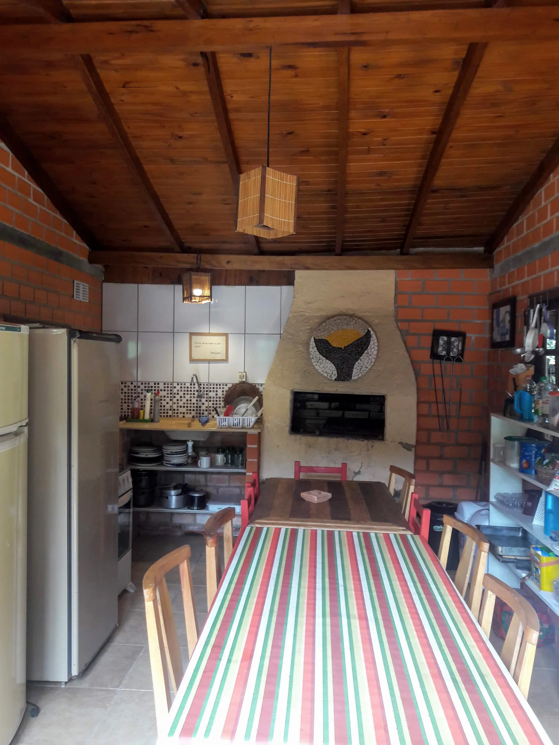 Cozinha alternativa com churrasqueira, geladeiras e mesa comprida com toalha listrada