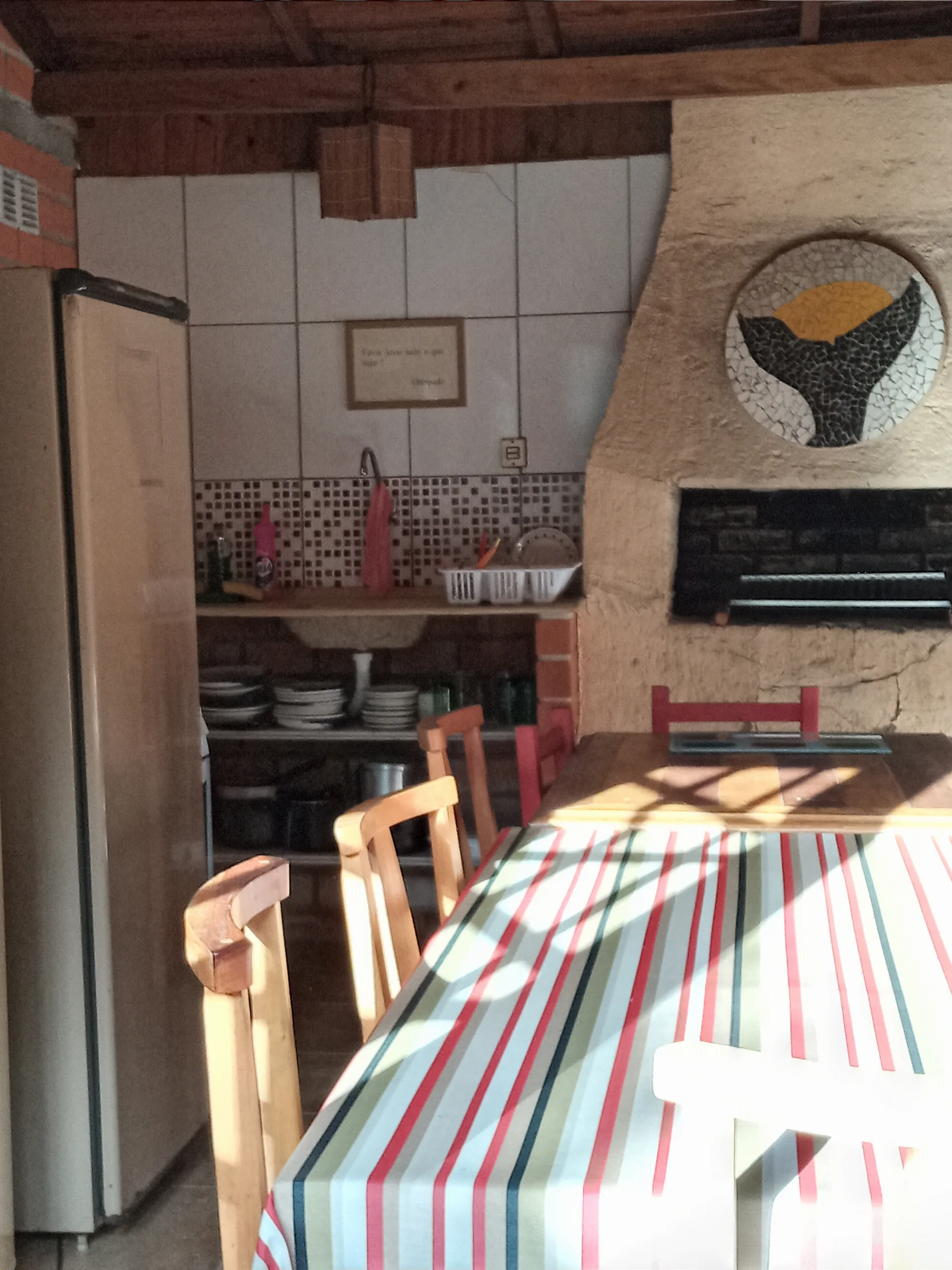 Mesa da cozinha alternativa com toalha listrada, pia e churrasqueira ao fundo