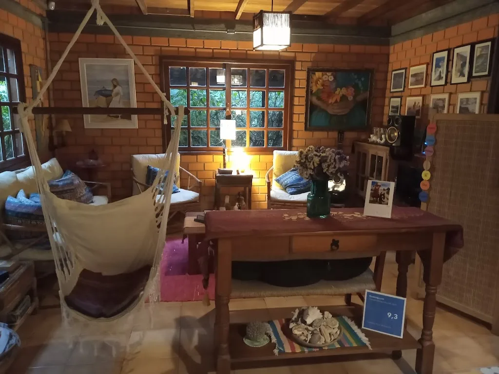 Sala de estar da pousada com cadeira de balanço, sofás, livros e quadros