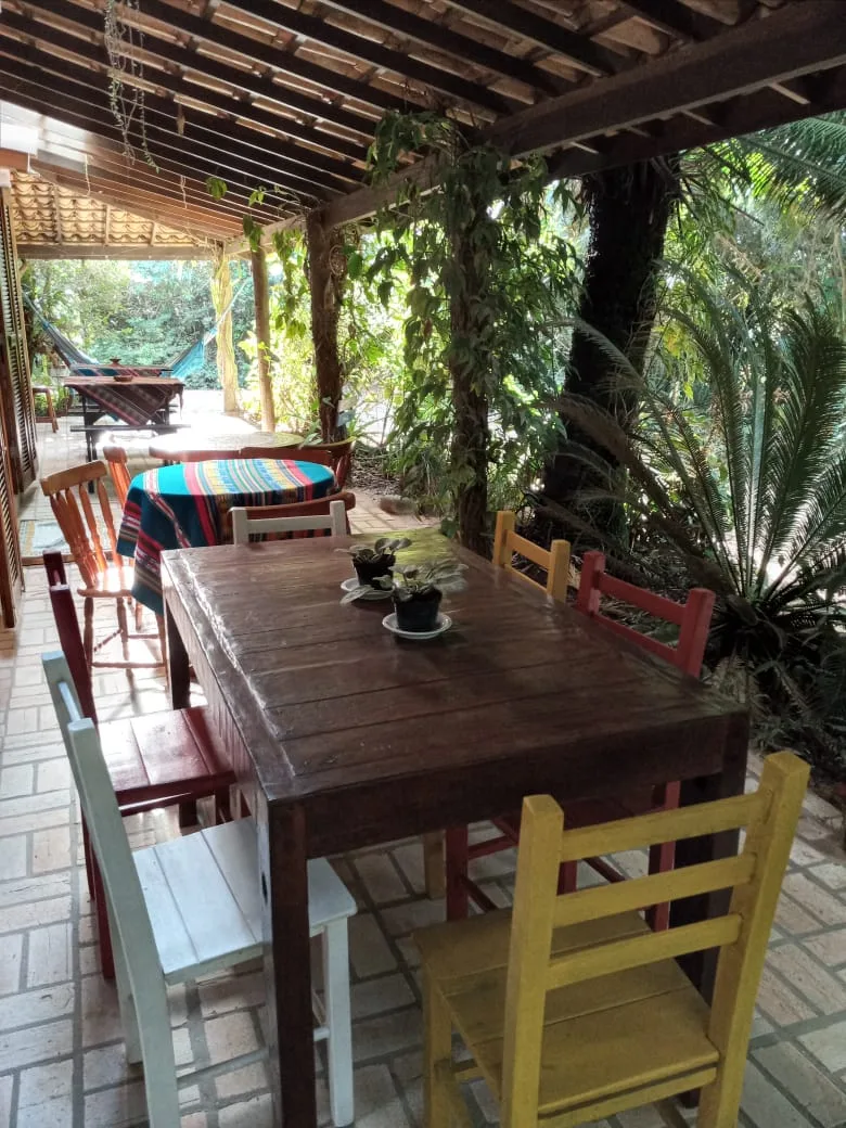 Mesa de madeira com cadeiras coloridas na varanda, em meio ao verde do jardim